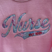Pink shirt with floral 'Nurse' text and 'EST 2028' on a pink background