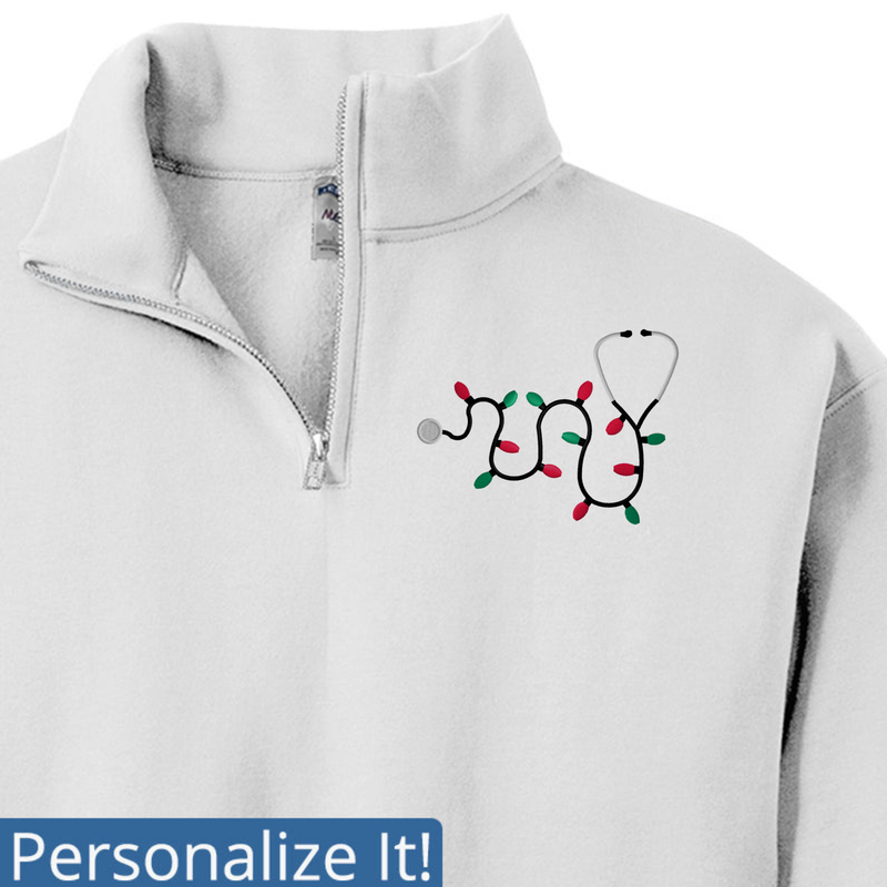 White quarter-zip sweatshirt with a stethoscope and Christmas lights design on a white background.